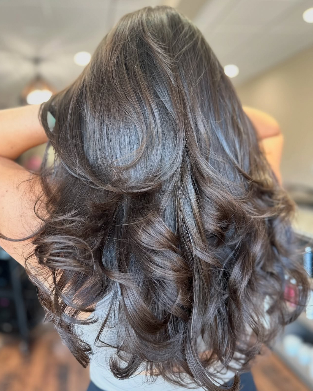 Close-up image of person's shiny, wavy, brown hair with highlights, styled in loose curls.