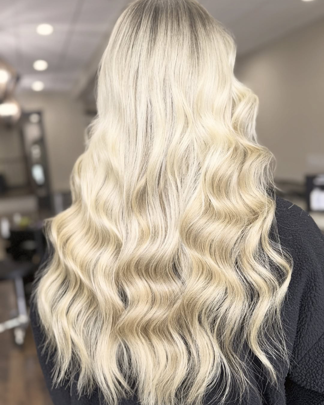 Long, wavy blonde hair on a person, shown from the back in an indoor setting.