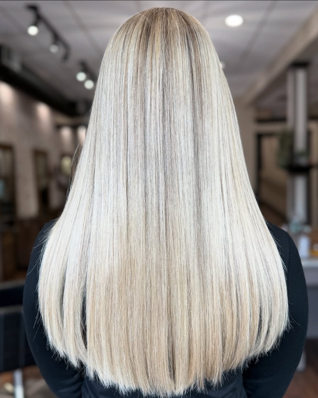 Back view of a woman with long, straight, platinum blonde hair in a salon.