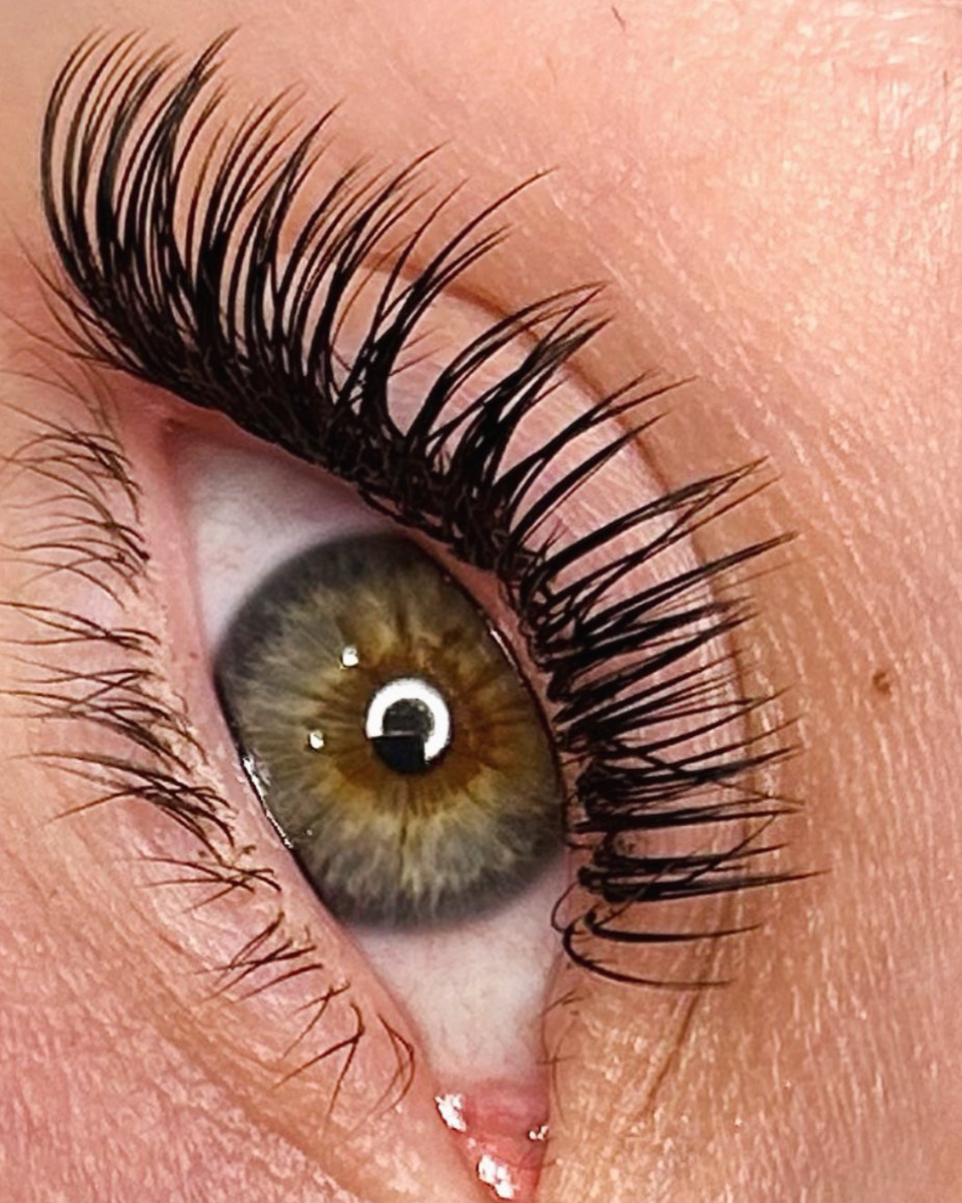 Close-up of a human eye with long black eyelashes, hazel iris, and a reflection of a light source in the eye.