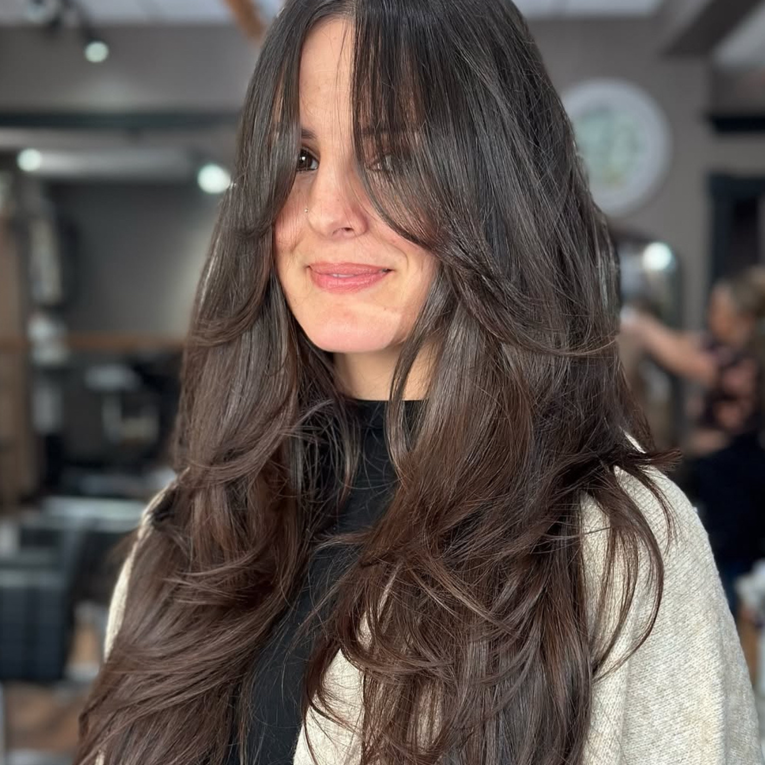 Portrait of a woman with long, wavy brown hair, smiling slightly, in a casual indoor setting.