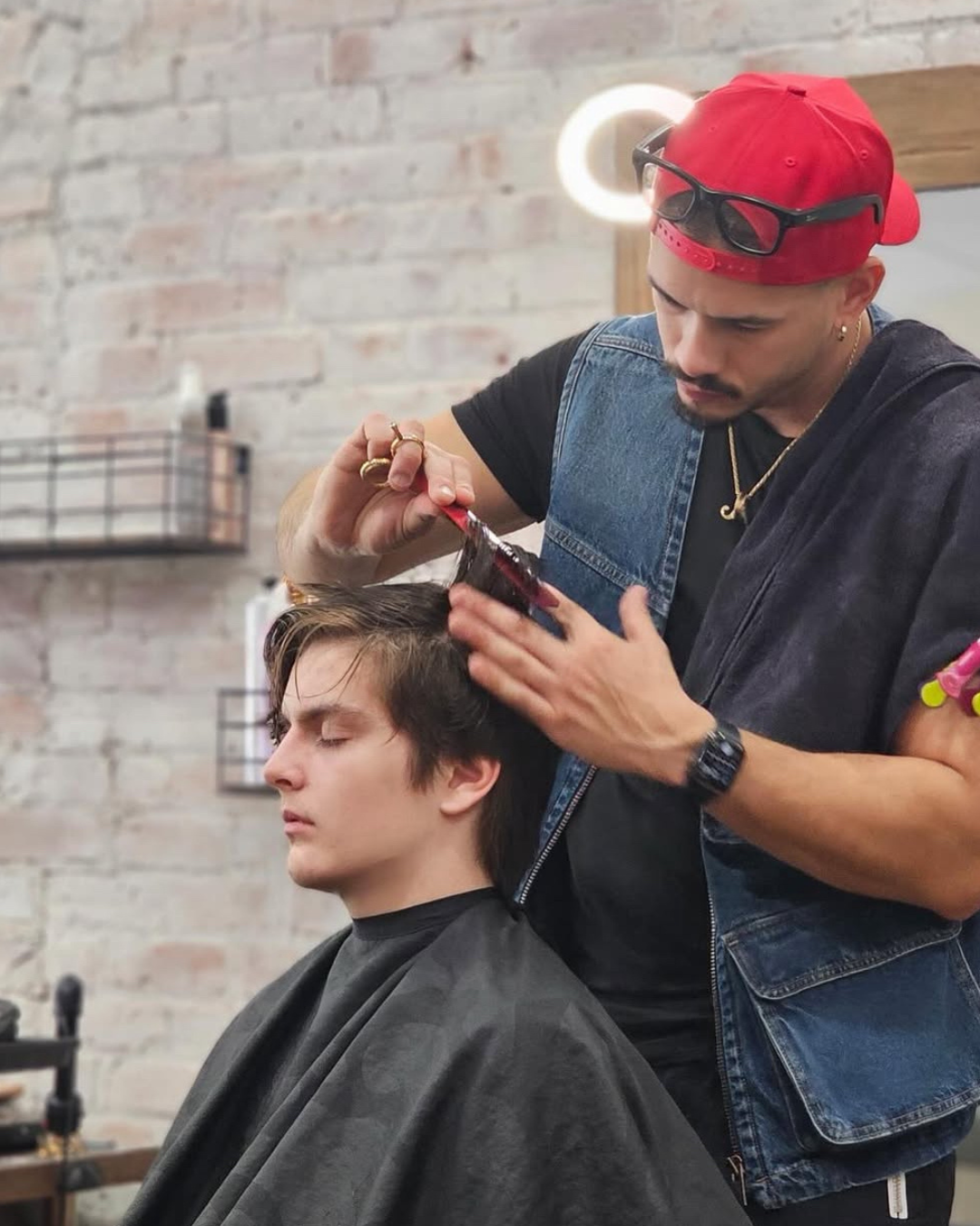 Barber applying hair dye to a male client in a salon.