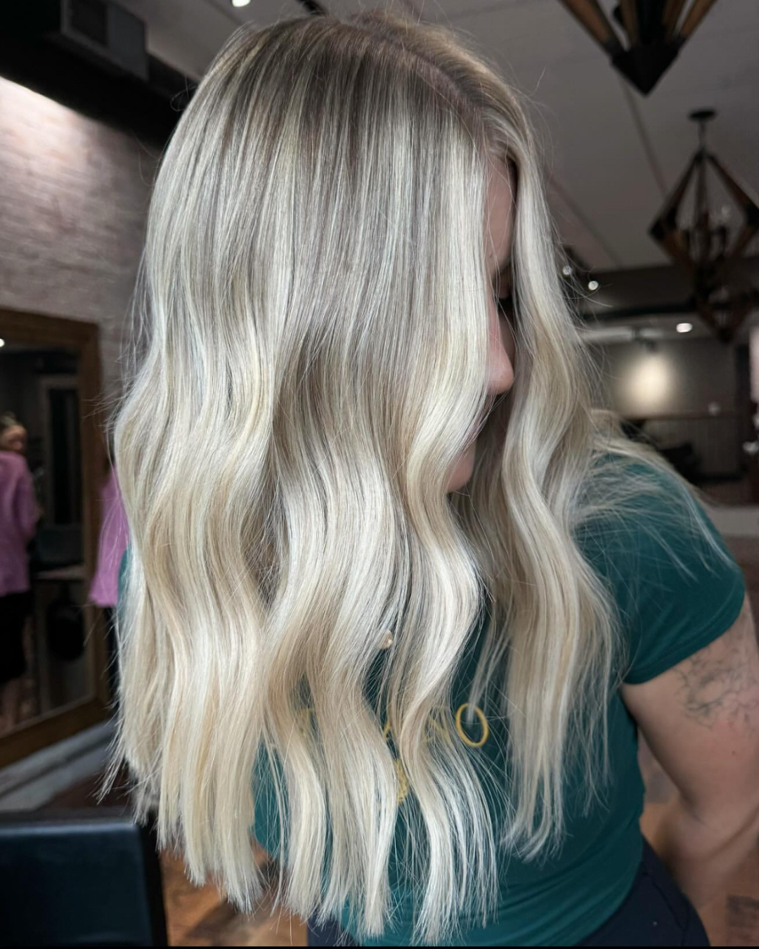 Close-up of a woman with long, wavy platinum blonde hair, partially covering her face, in a salon setting.