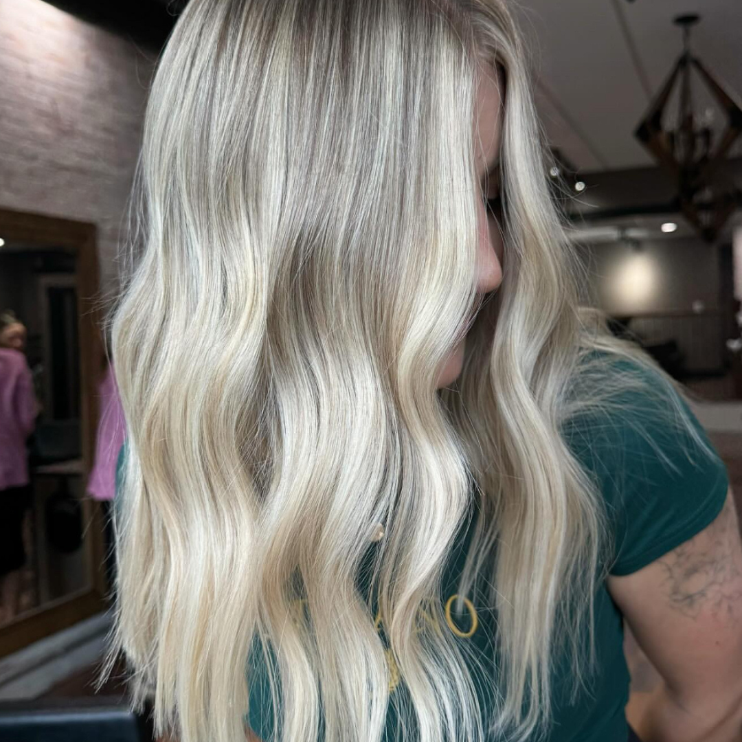 Close-up of a woman with long, wavy blonde hair, in a salon or indoor setting.