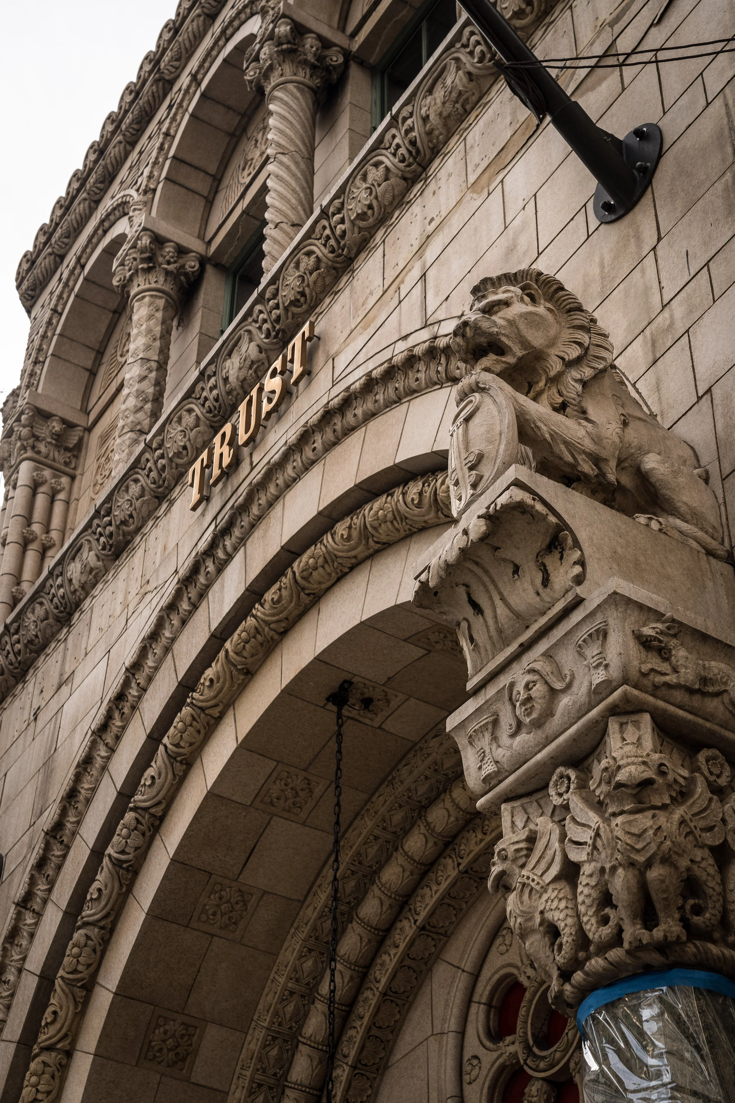Close-up of a historic stone building with intricate carvings, including a lion and a fierce face, and a sign that says 'TRUST'.