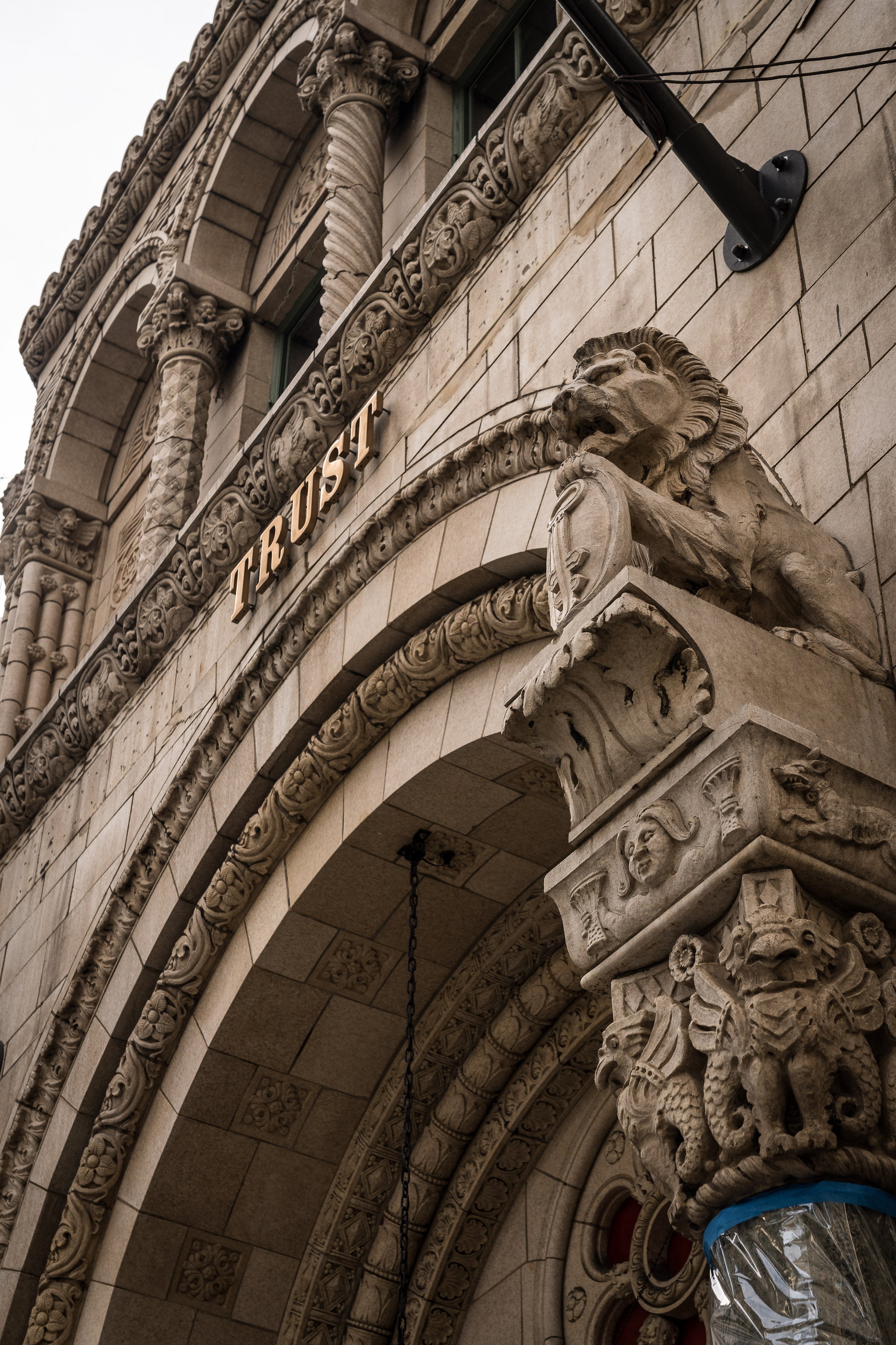 Close-up of ornate stone facade of a historic building with detailed carvings, lion and other sculptures, and the word "TRUST" in gold lettering.