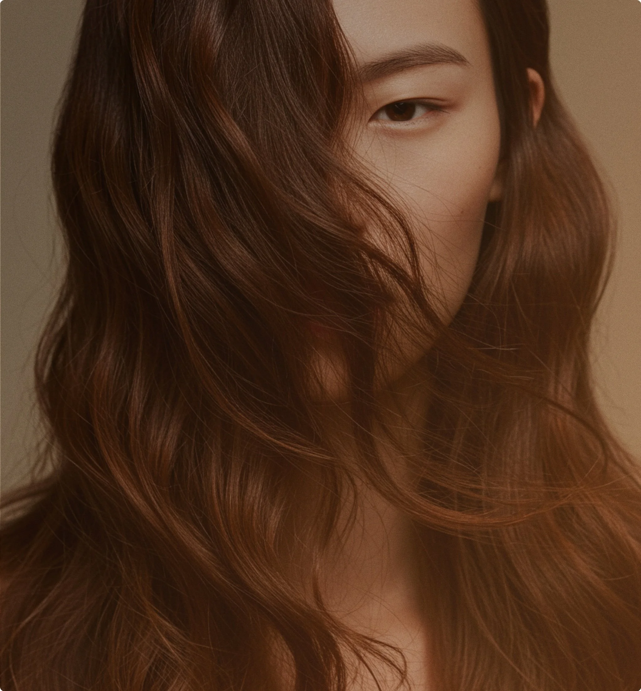 A woman with long wavy auburn hair covering part of her face, showing only her eye, eyebrow, and part of her nose.