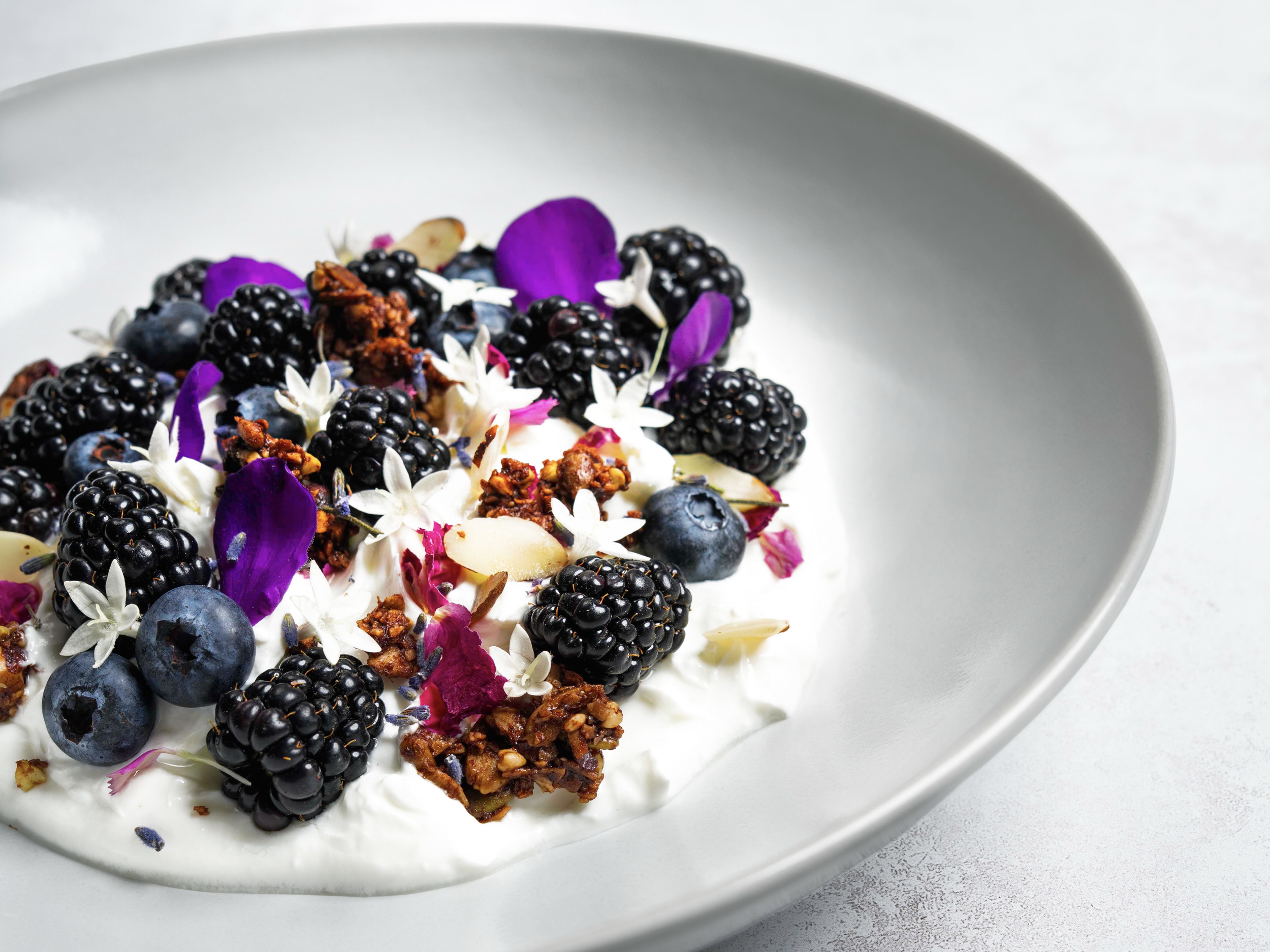 A bowl of yogurt topped with blackberries, blueberries, edible flowers, and granola.