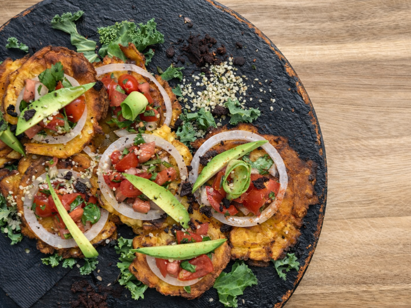 Chiles Rellenos topped with diced tomatoes, onions, and avocado slices, served on a black slate platter with herbs and sesame seeds.