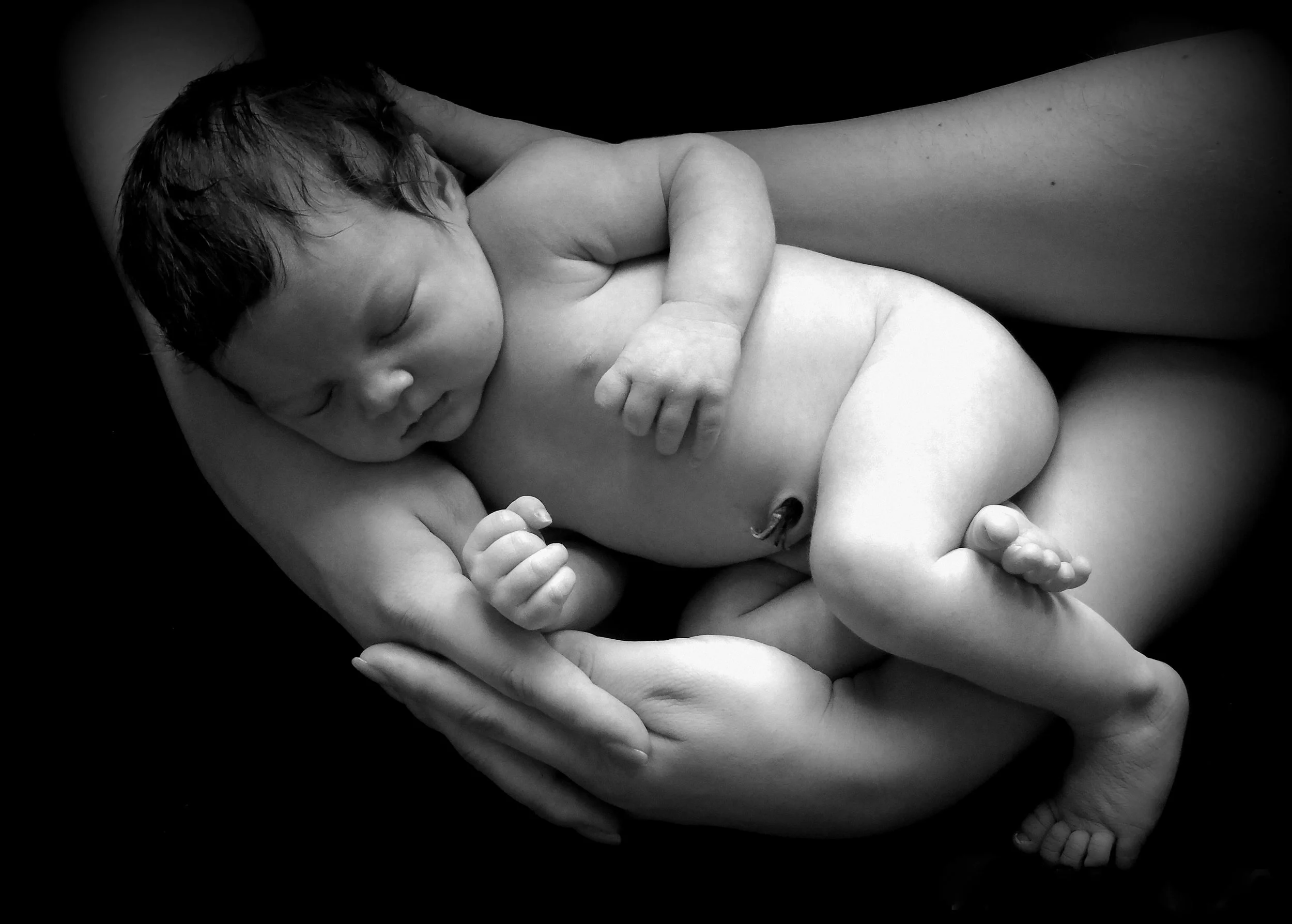 Black and white photo of a newborn baby sleeping cradled in an adult's hands and arms.
