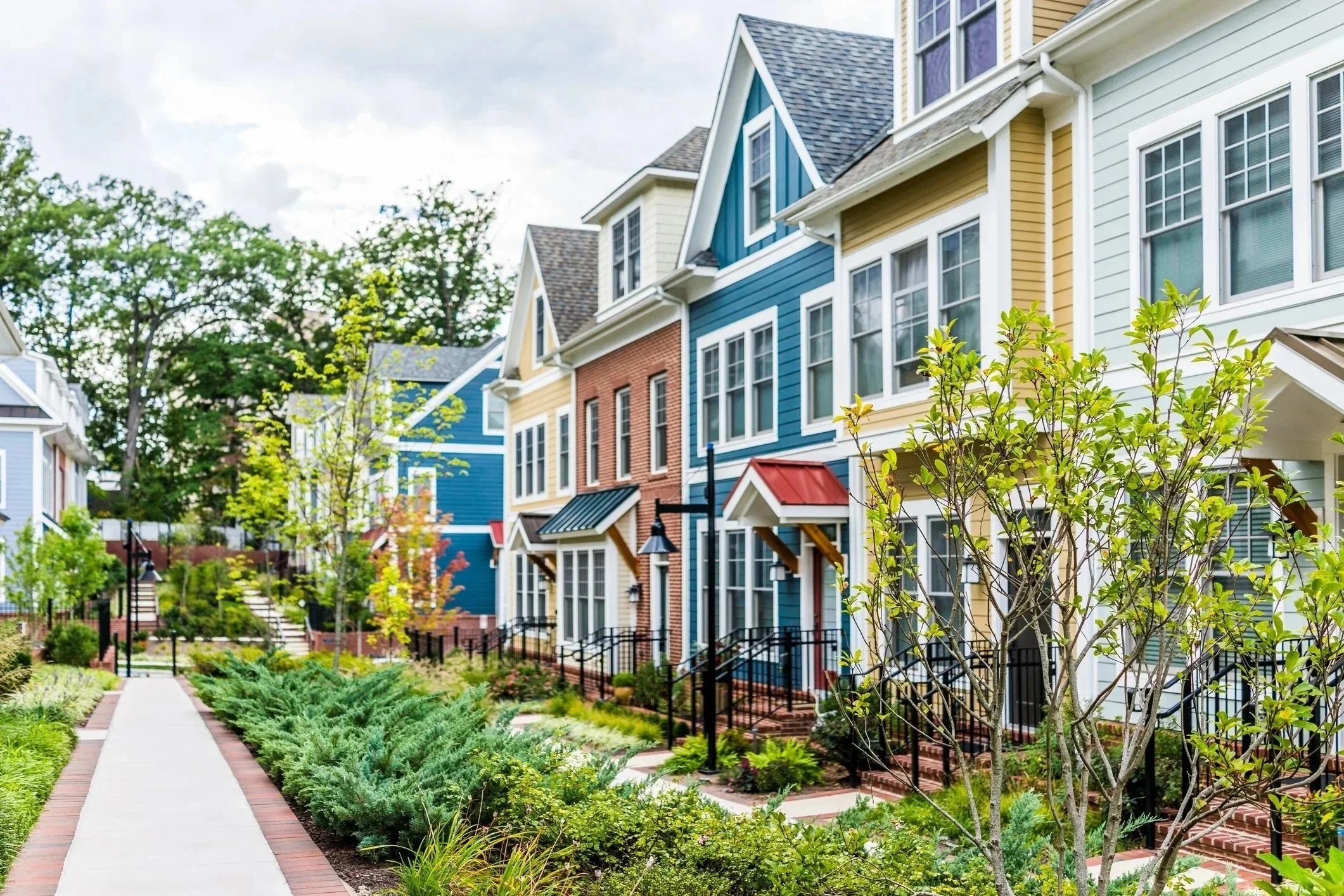 Colorful row of modern townhouses with landscaped front yards and a sidewalk in a suburban neighborhood.