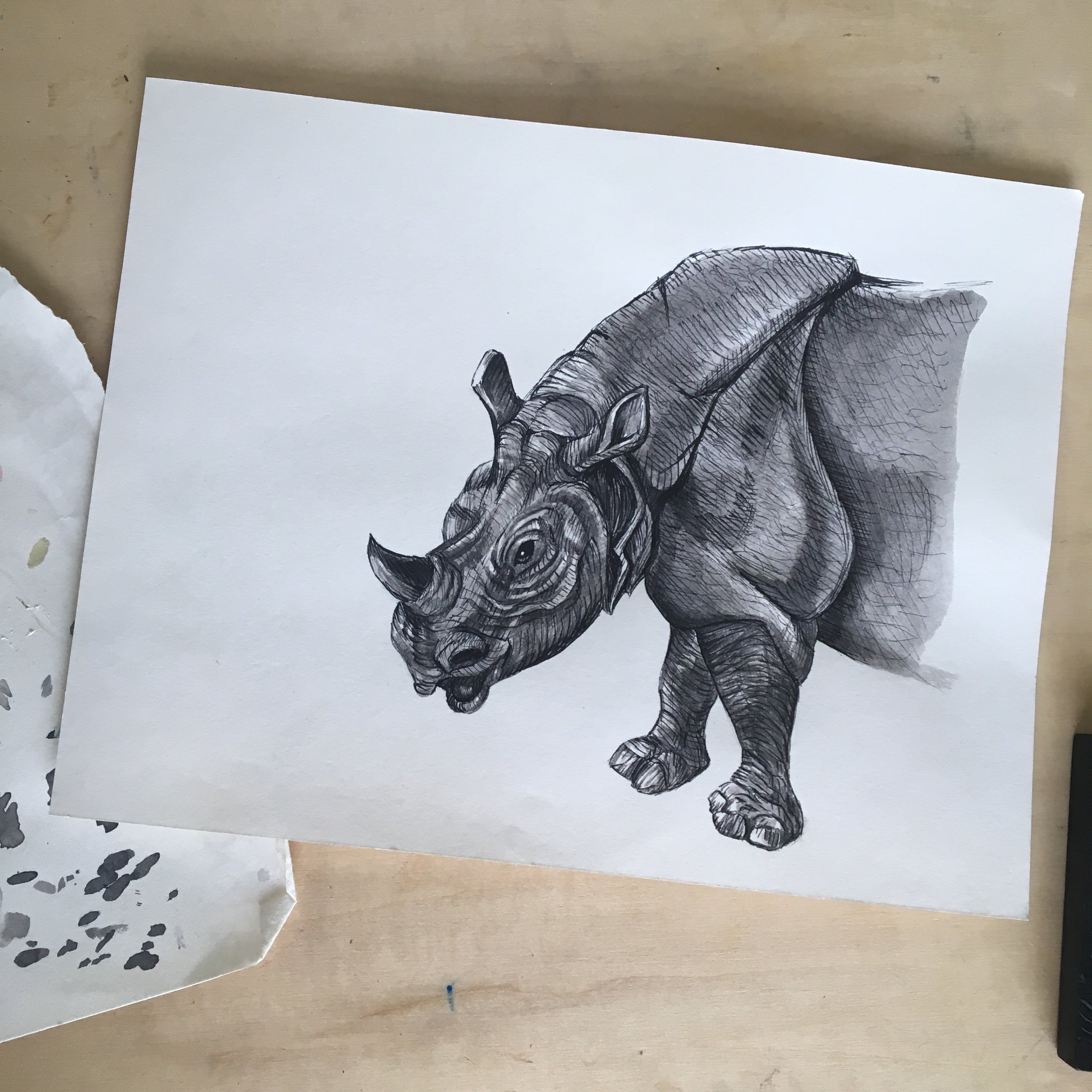A detailed black and white drawing of a rhinoceros on a white sheet of paper.