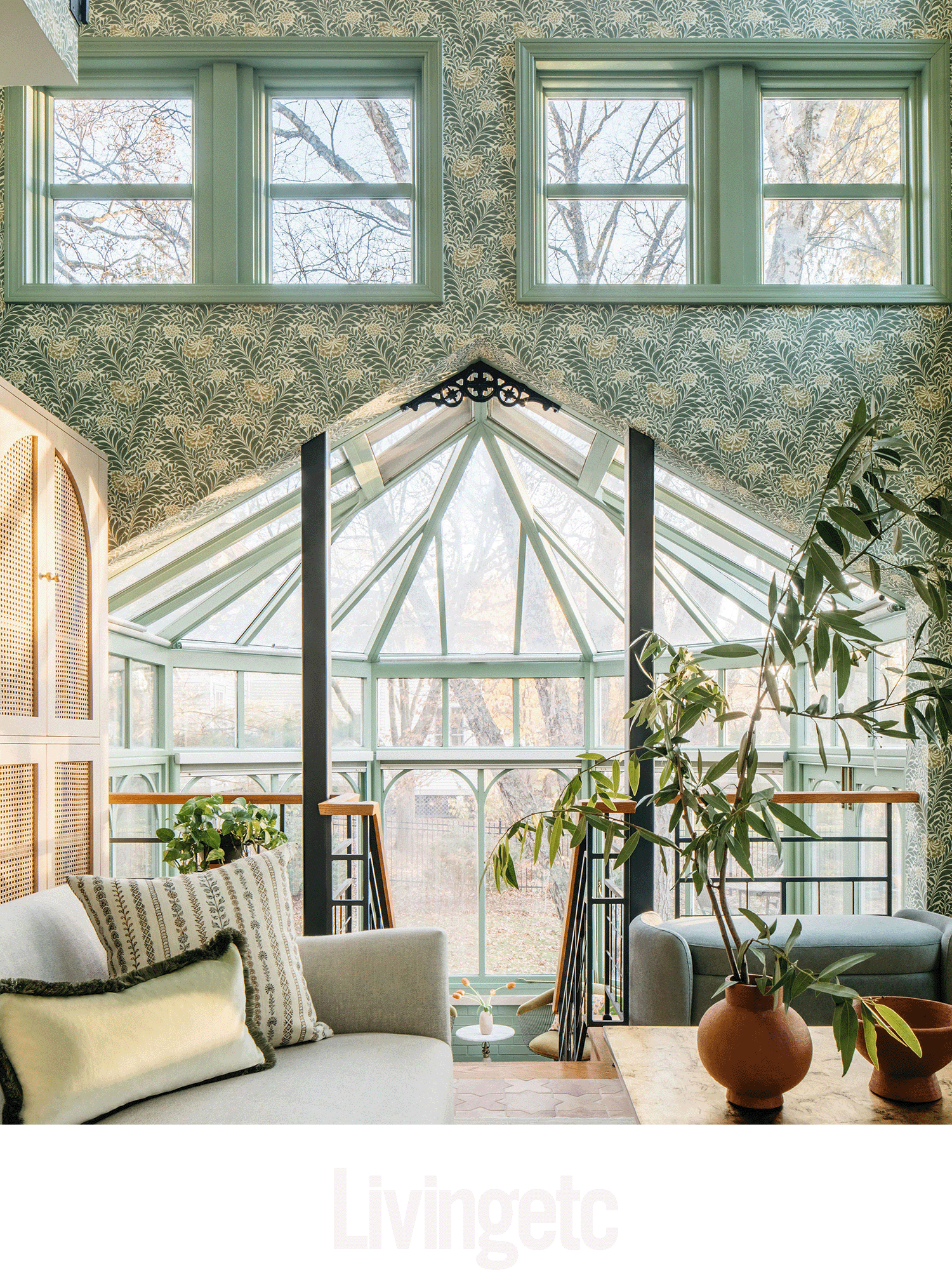Sunlit living room with large glass windows and a glass ceiling, furniture, and indoor plants.