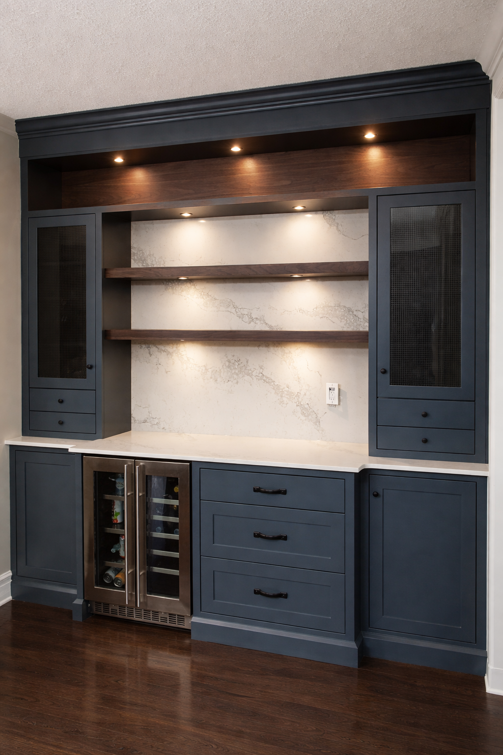 Built-in dark blue cabinets with glass-front mini fridge, open shelves, and closed drawers, with a white marble countertop in a home kitchen or bar area.