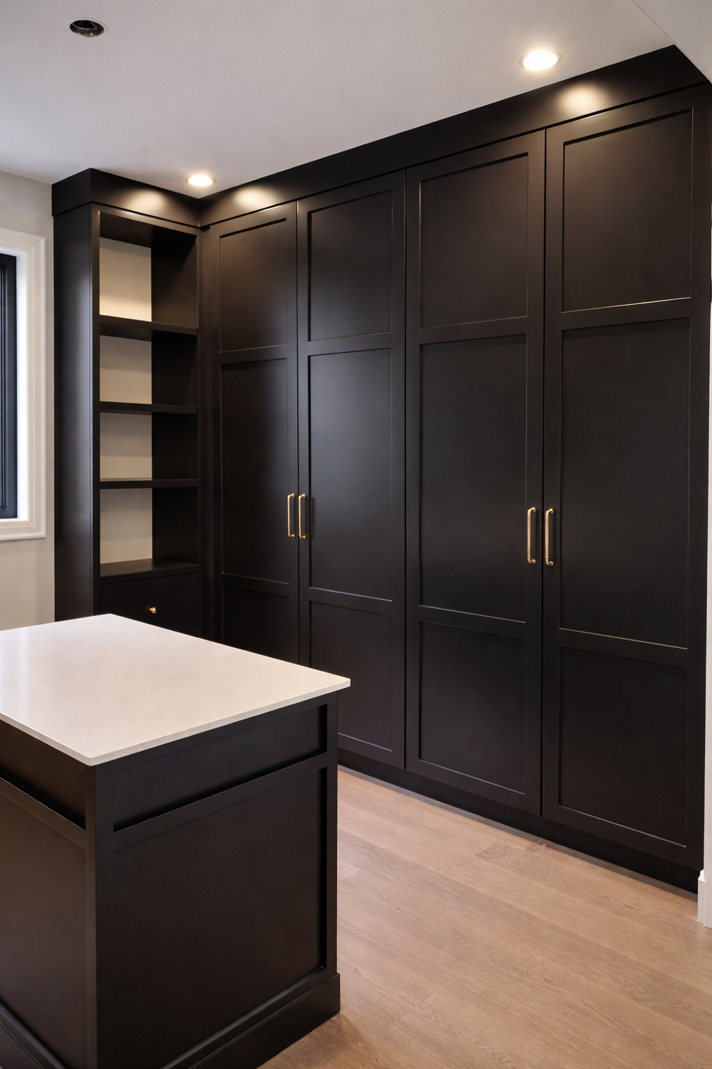 A modern kitchen with black cabinets, a white countertop island, wooden flooring, and recessed ceiling lights.