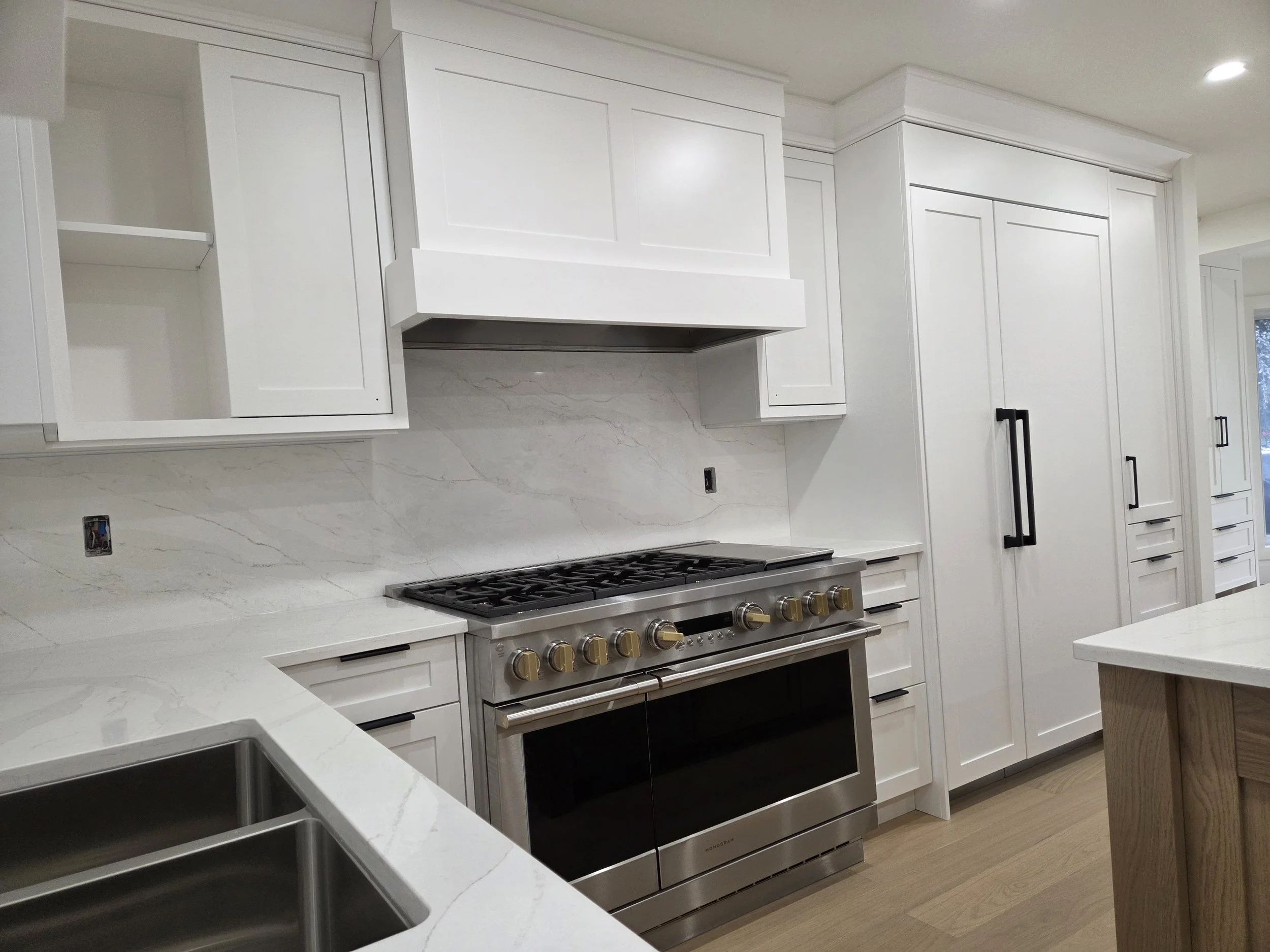 Modern kitchen with white cabinetry, a stainless steel oven and stove, marble countertops, and a wooden island.