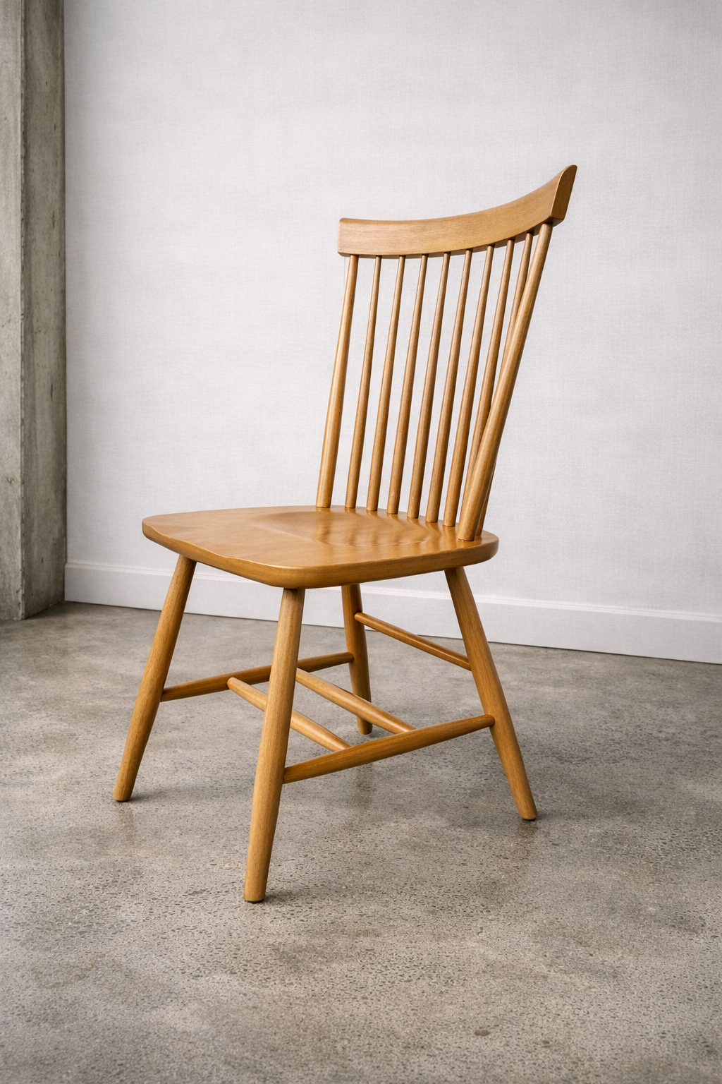 A wooden chair with a high back and vertical slats, placed on a concrete floor against a white wall.
