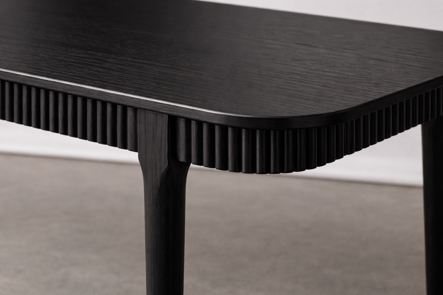 Close-up of a black wooden table corner with ribbed edging and curved leg.