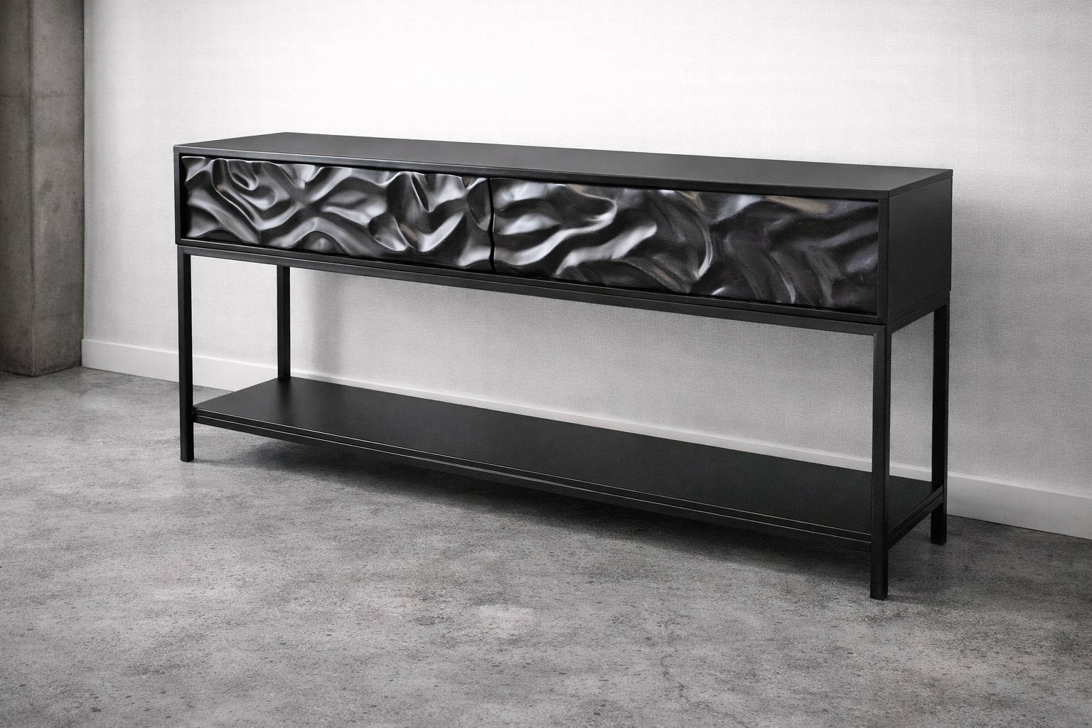 A modern black console table with a metallic, textured drawer front and a lower shelf, positioned against a light-colored wall and next to a concrete column.