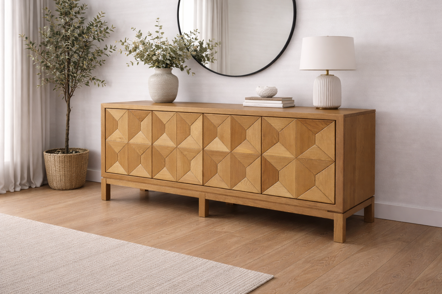 A wooden sideboard with geometric patterned doors in a living room with light-colored walls and hardwood flooring. Decorative items, including a vase with greenery, a table lamp, a few books, and a bowl, are placed on top of the sideboard. There's a large round mirror on the wall above the sideboard and a tall potted plant with broad leaves near the corner.