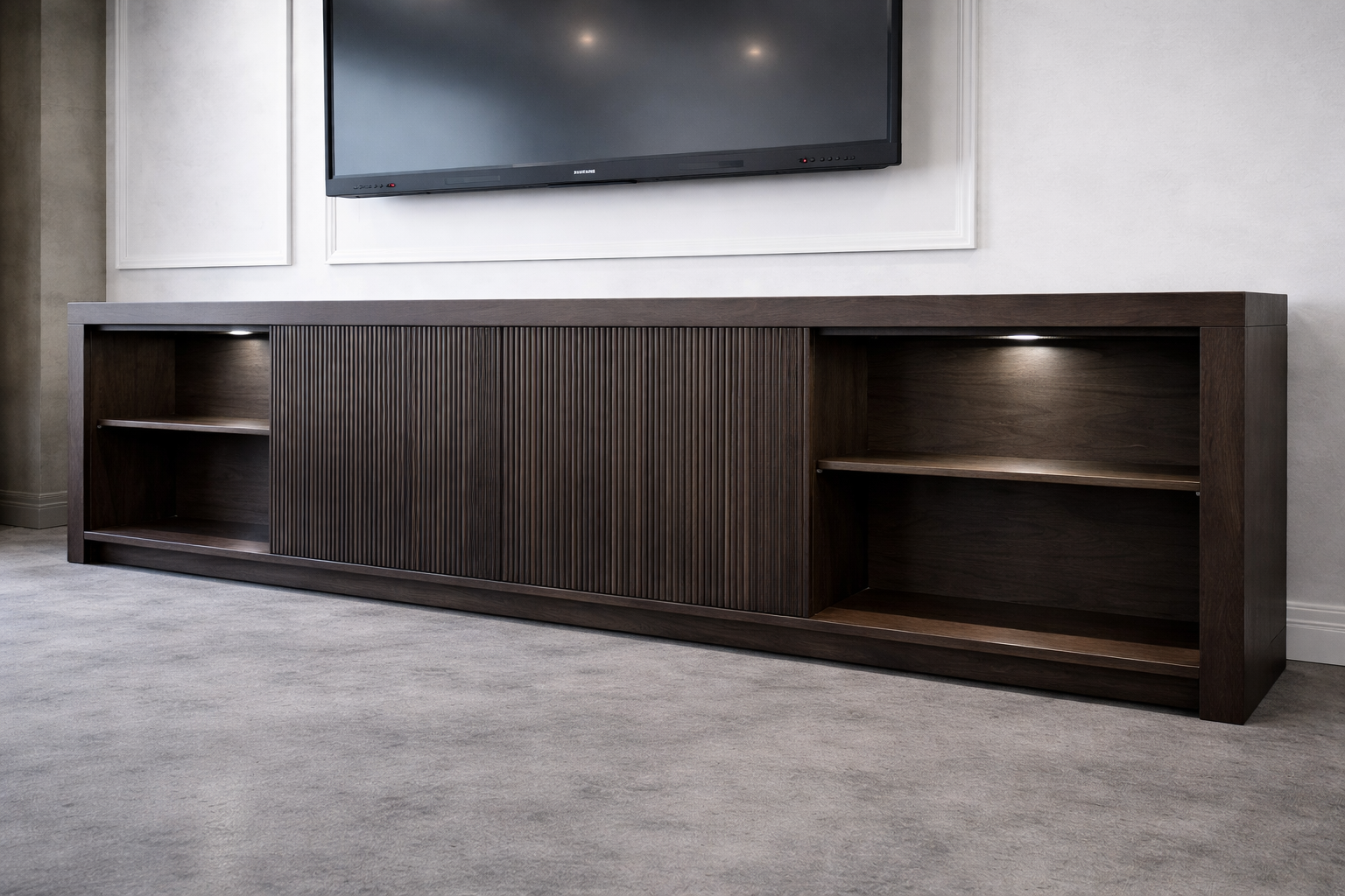 Dark brown wooden TV stand with open shelves on each side and a sliding door section in the middle, placed against a white wall with a mounted flat-screen TV above.