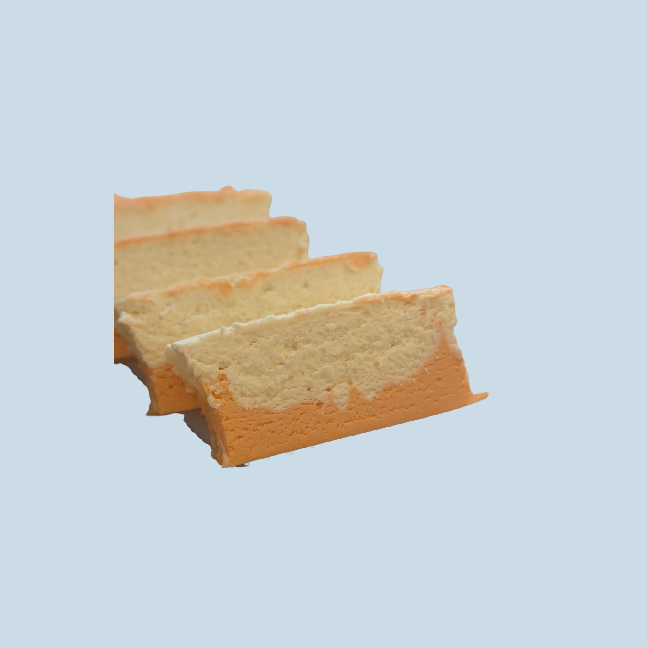 Three slices of orange creamsicle fudge arranged in a row against a light blue background.