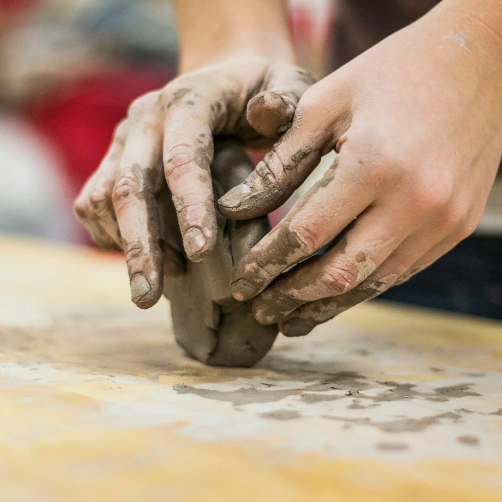 Close-up of hands kneading gray clay on a wooden surface.