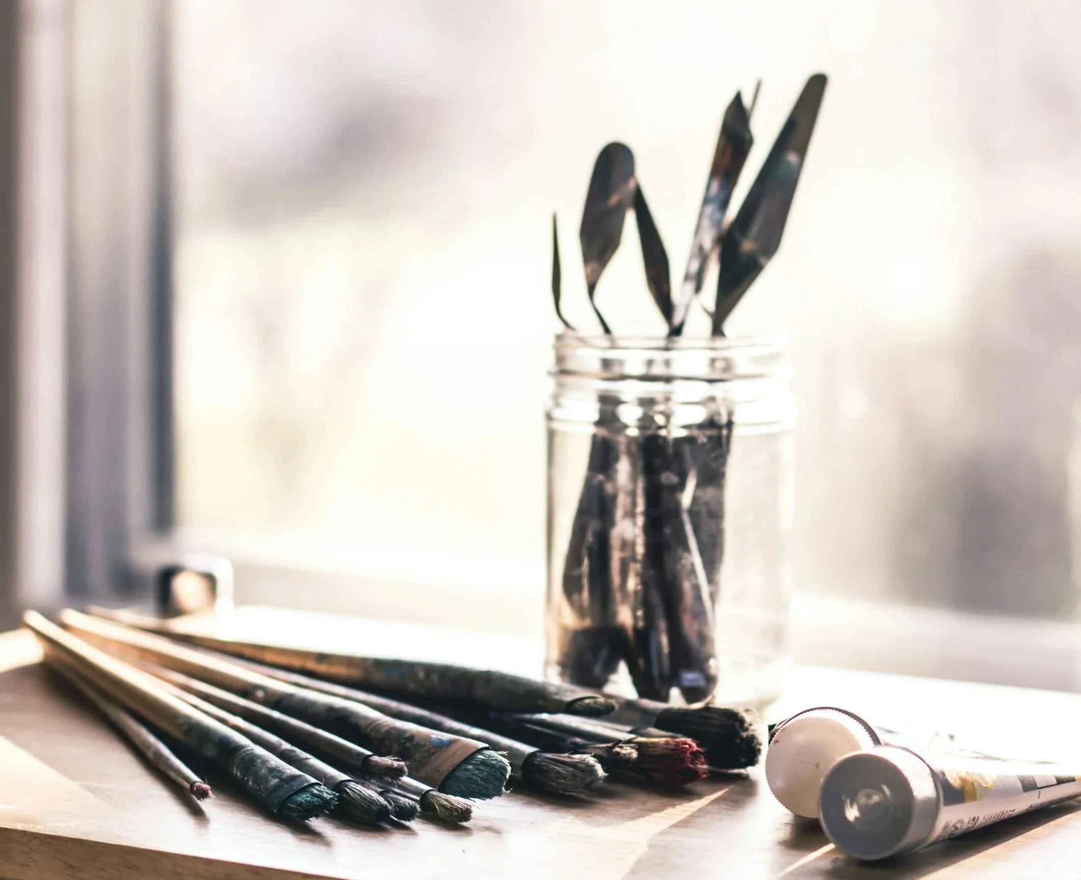 Paintbrushes and paint tube on a wooden table near a window