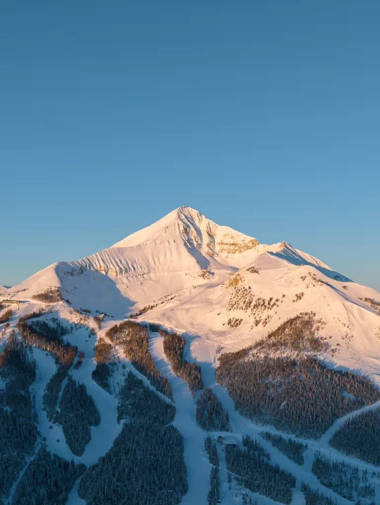 Snow-covered mountain with a ski resort and ski trails, under a clear blue sky.