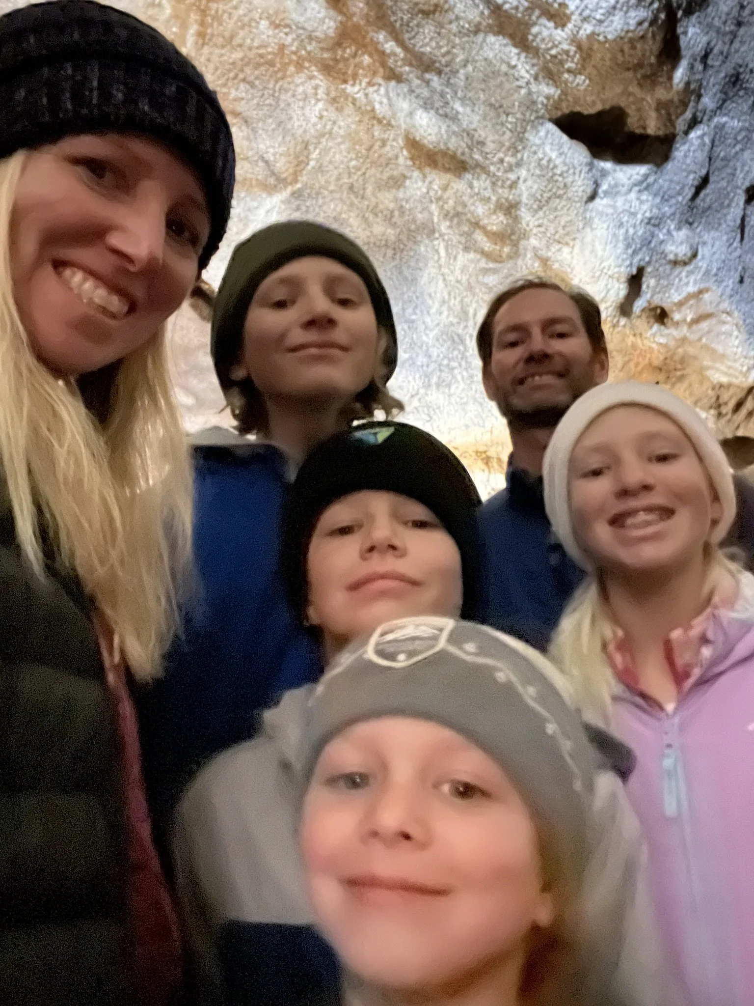 A group of six people, including two adults and four children, taking a selfie inside a cave with rocky walls.