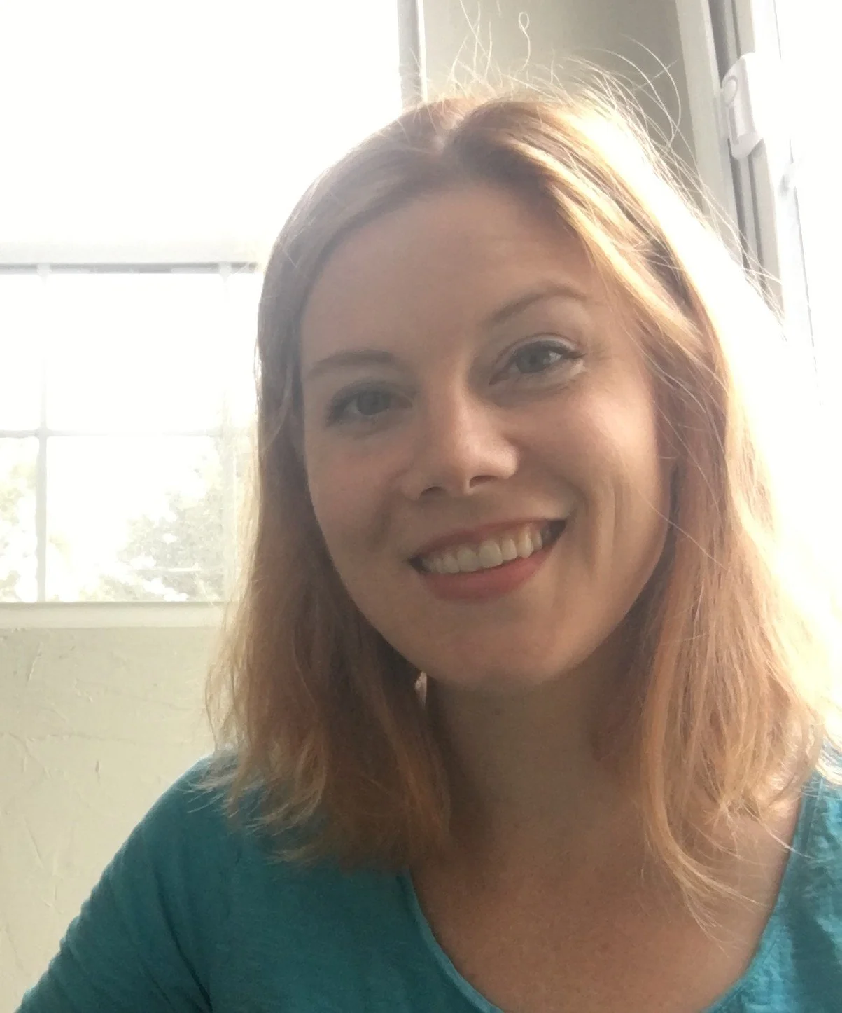 A young man in a gray polo shirt and beige pants sitting on a beige cushioned bench against a plain light-colored wall, with soft shadow cast on the wall.