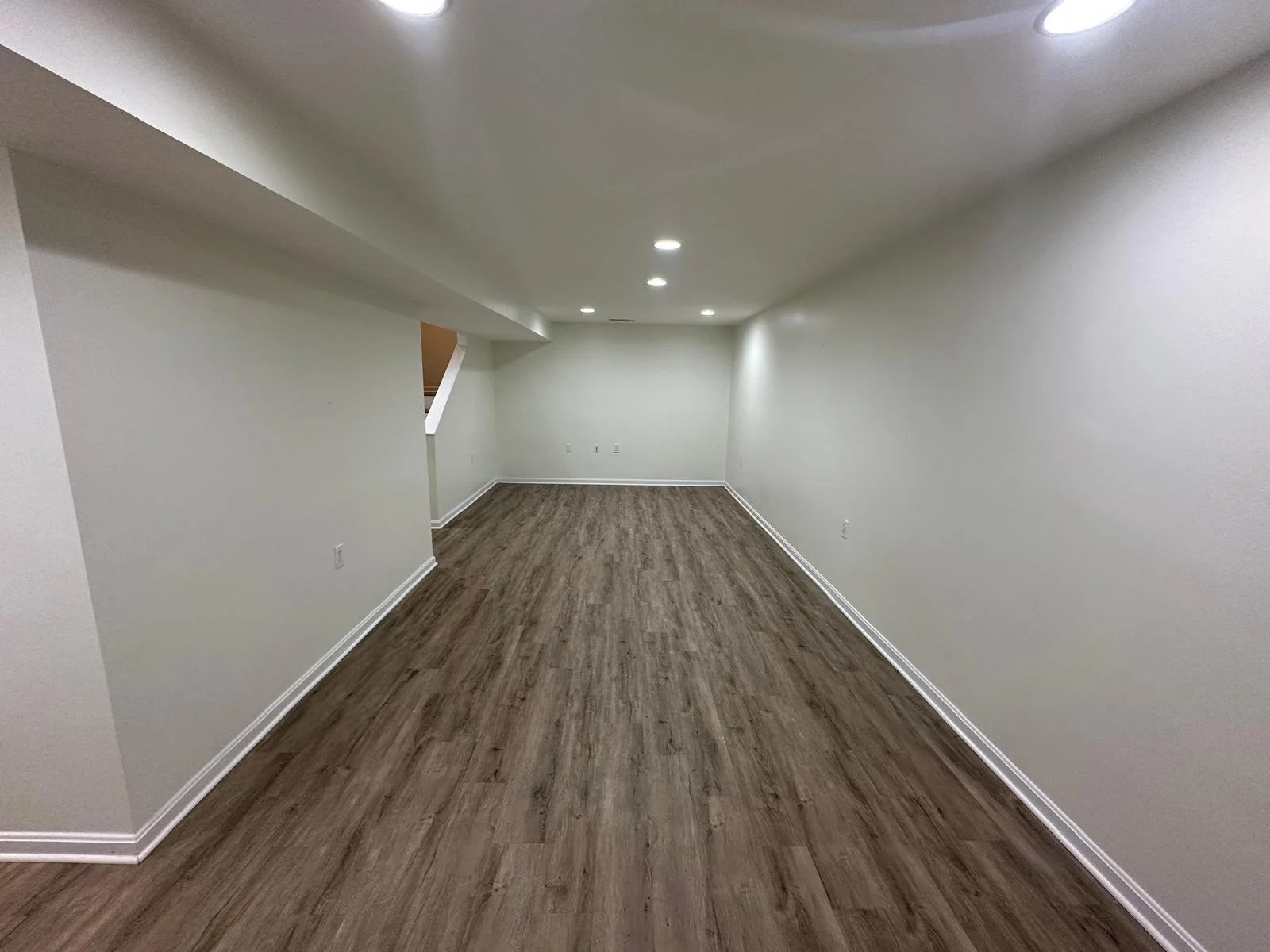 Empty rectangular room with white walls, wood vinyl flooring, and ceiling recessed lights.