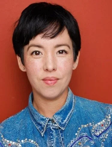 Woman with short black hair wearing a denim jacket against a red background.