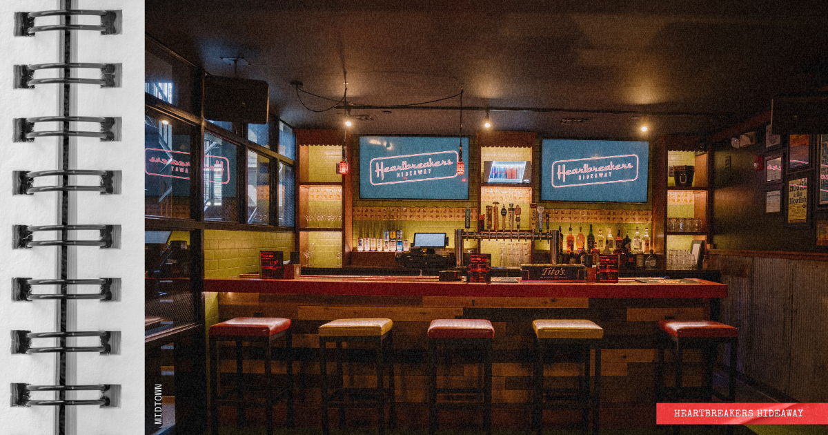 Empty bar with five stools in front, two digital screens displaying 'Heartbreakers Hideaway', bottles of alcohol behind the bar, and dim lighting.