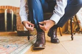 Person tying shoelaces on a brown boot while kneeling on a rug in a living room.