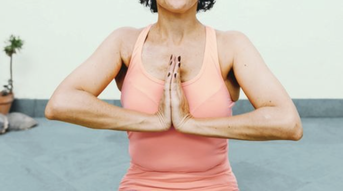 A woman practicing yoga outdoors, sitting cross-legged with hands in a prayer position.