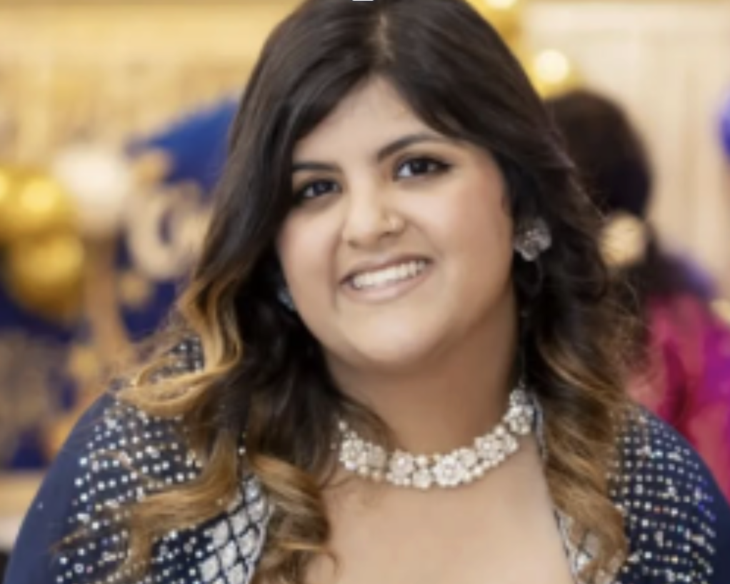 A woman smiling, dressed in formal attire with jewelry, at a celebration or event.