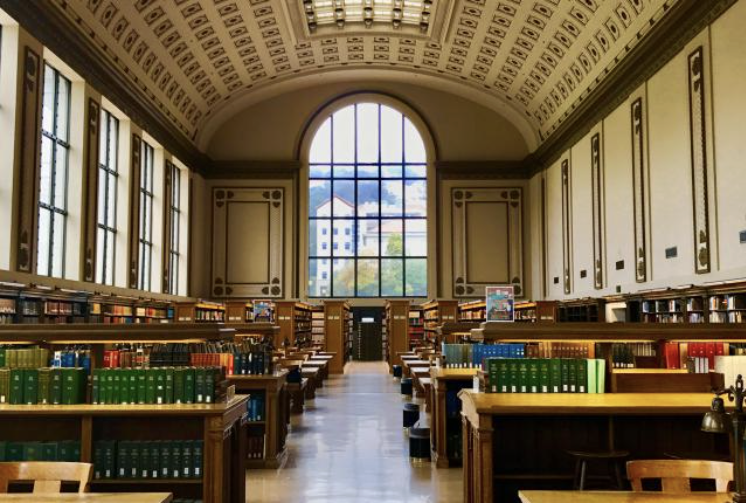 Interior of a historic library with high arched ceiling, large windows, and wooden bookshelves filled with colorful books.