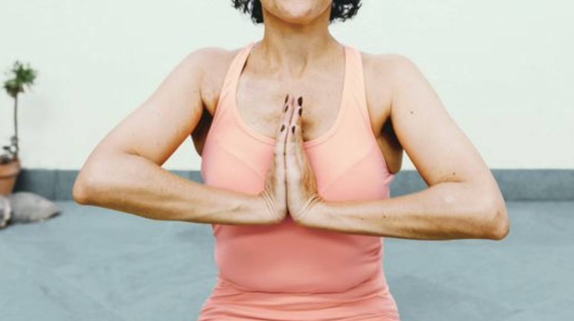 A woman practicing yoga indoors with her hands in prayer position at her chest.