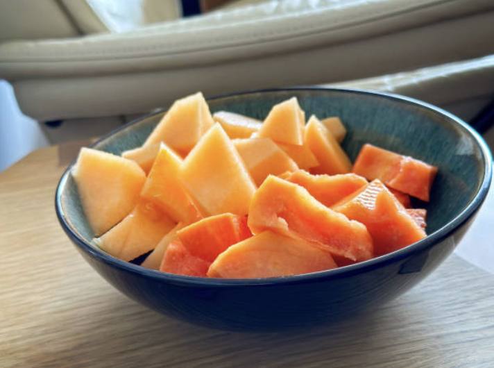 A blue bowl filled with sliced cantaloupe and watermelon on a wooden surface near a window.