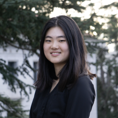 Young woman with shoulder-length black hair smiling outdoors with trees in the background.