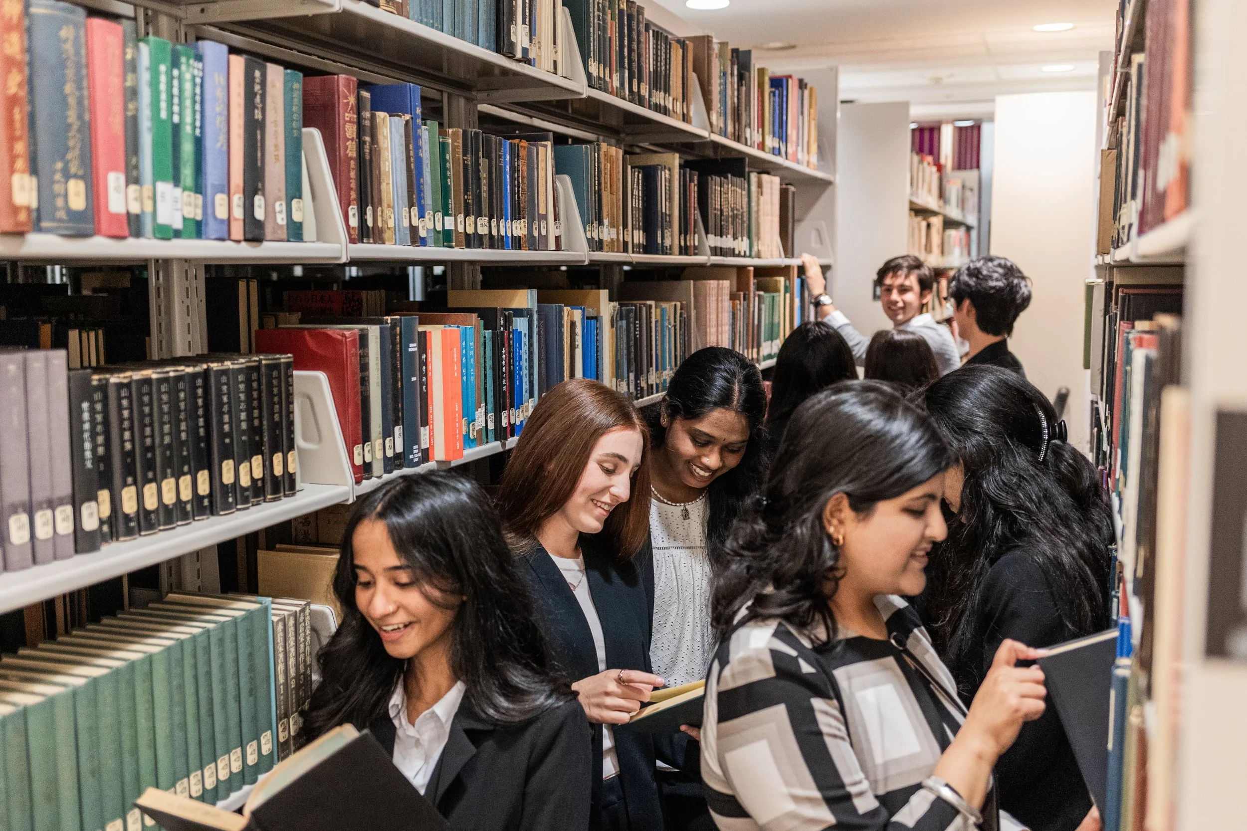 Group of diverse students shopping for books in a library aisle, looking at and selecting books from the shelves.