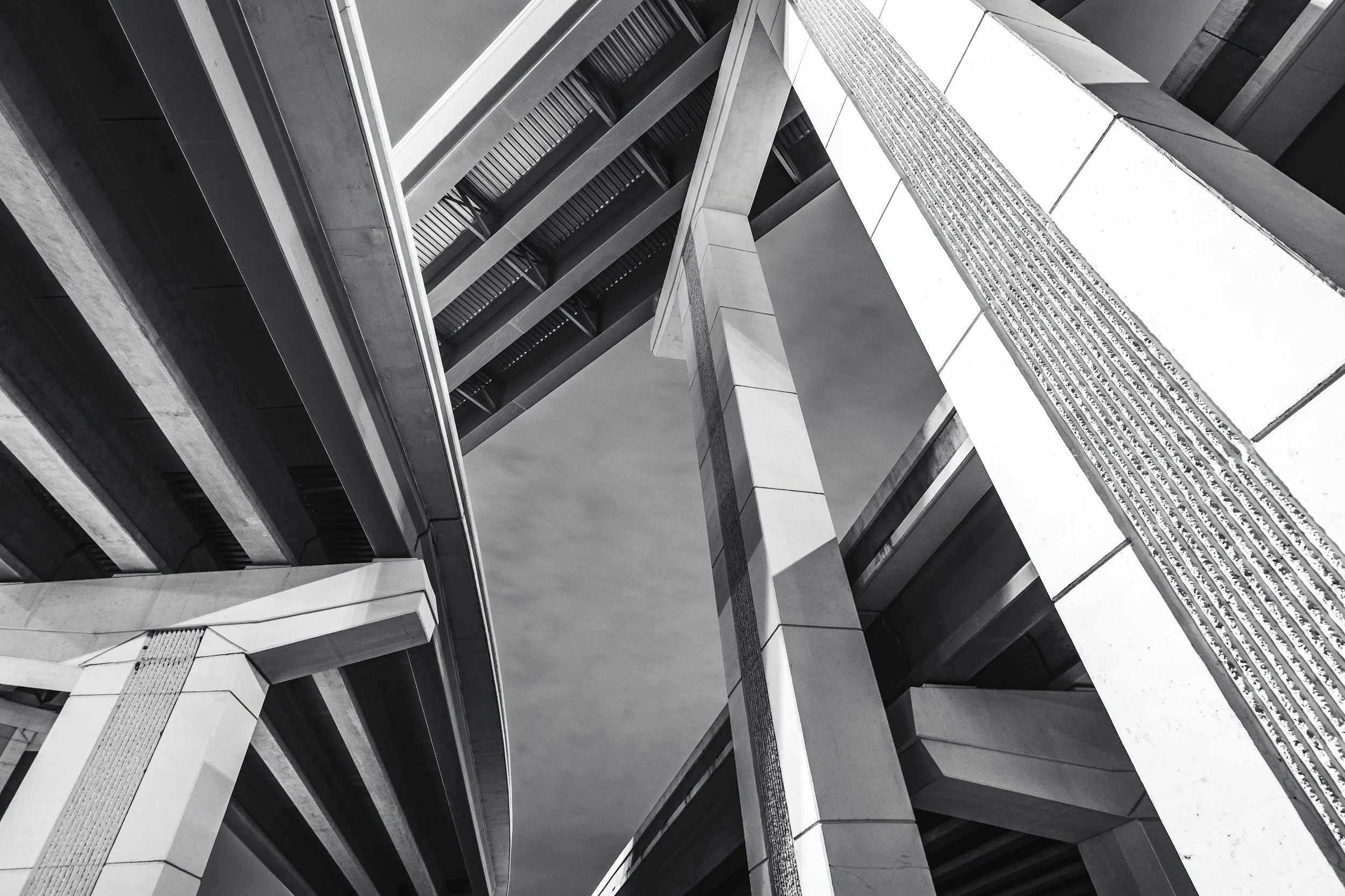 Black and white photo of modern concrete skyscraper with multiple levels and structural beams seen from below.