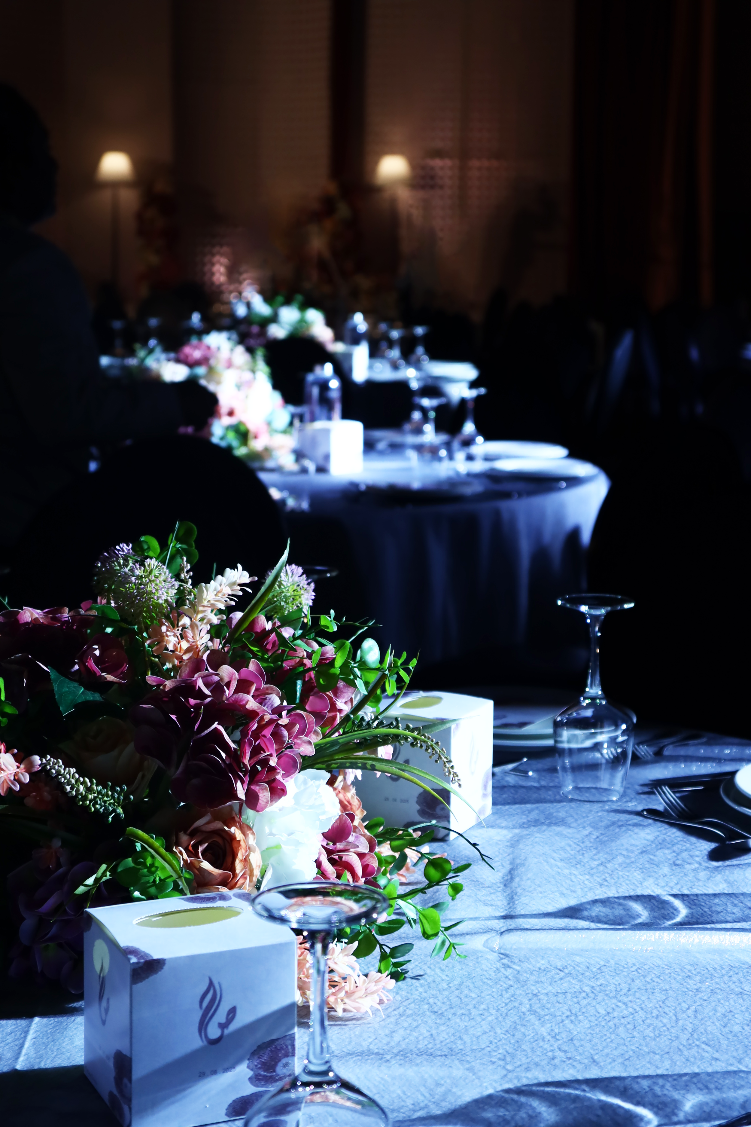 Table setting with a floral centerpiece, upside-down wine glass, and napkins in a dimly lit event space.