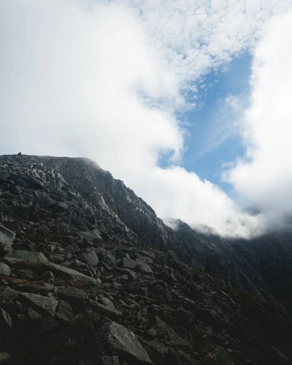 Rocky mountain slope with clouds and blue sky above.