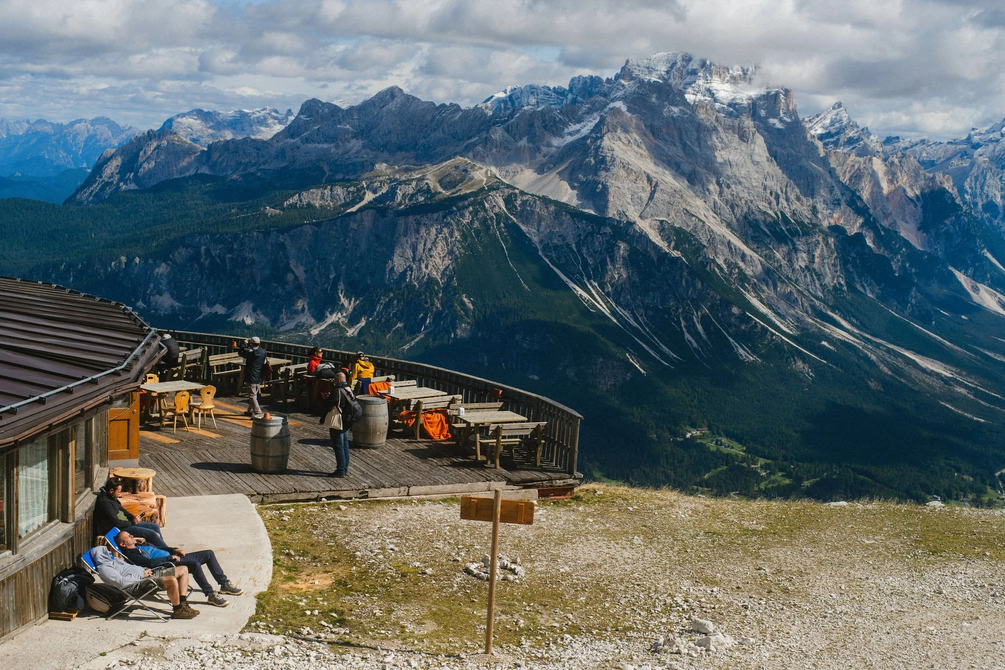 People relaxing and enjoying the scenic mountain view from a wooden terrace at a mountain lodge.