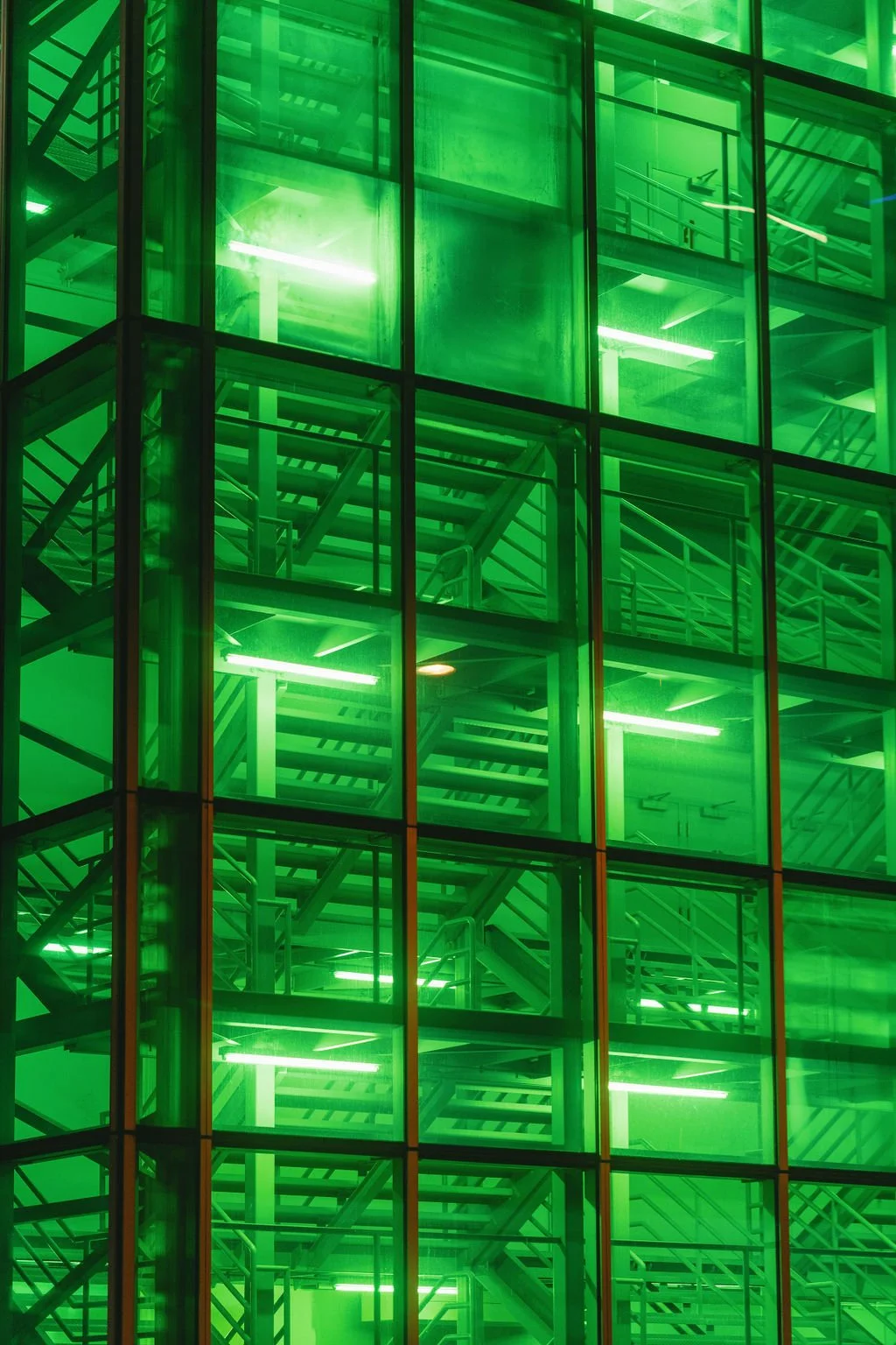 Green-lit modern glass building with visible staircases inside.