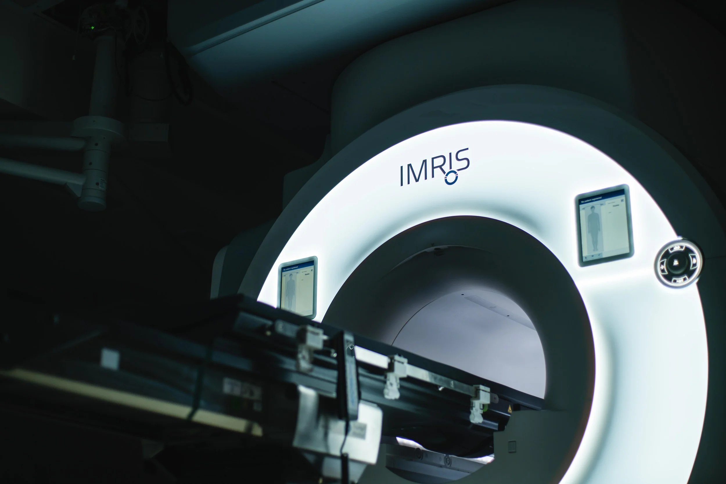 A large, illuminated medical imaging device with the brand name IMRIS, used for MRI scans, inside a hospital or medical facility.
