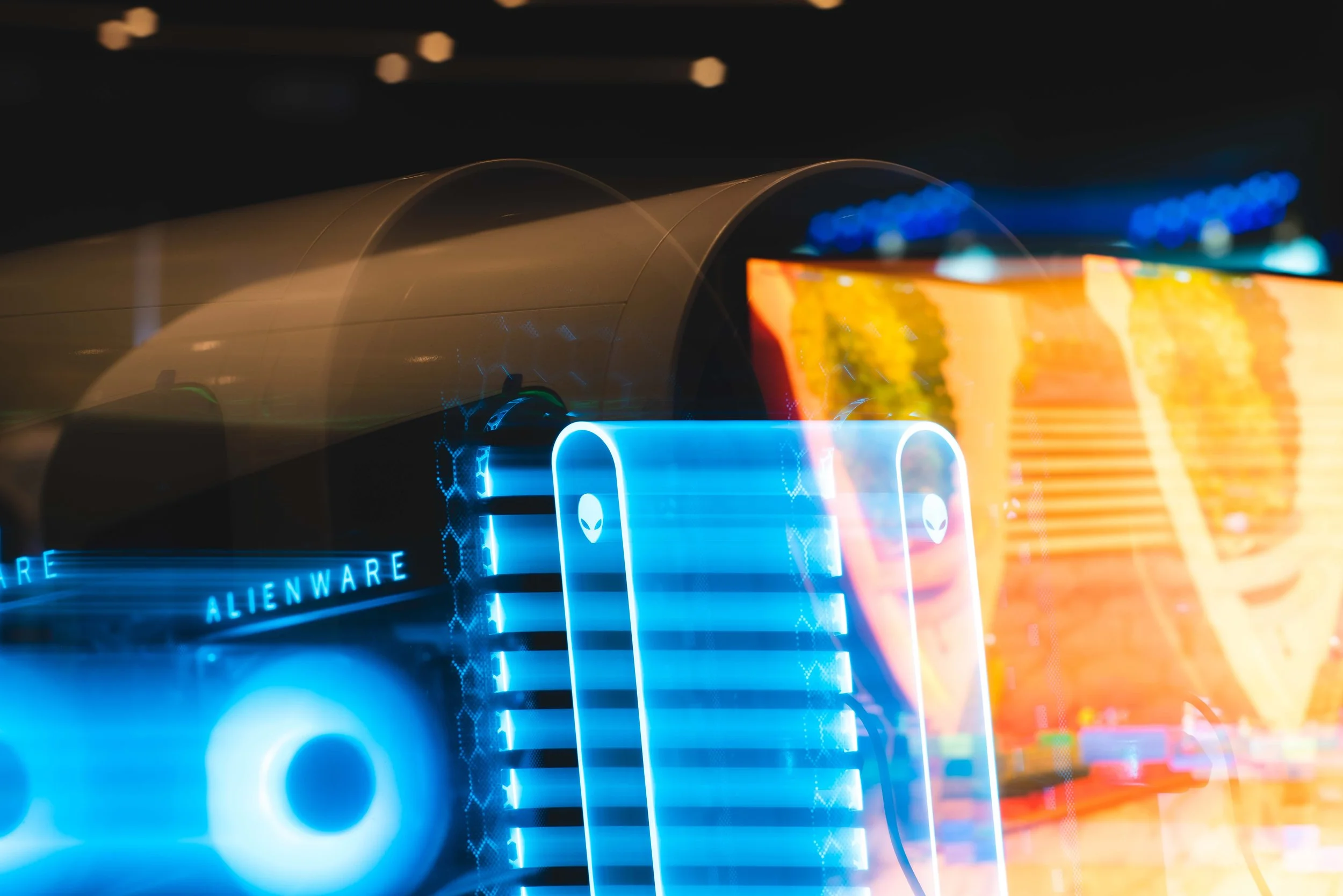 Close-up image of illuminated gaming computer components with the 'Alienware' logo in a dark room, featuring blue and orange lights.