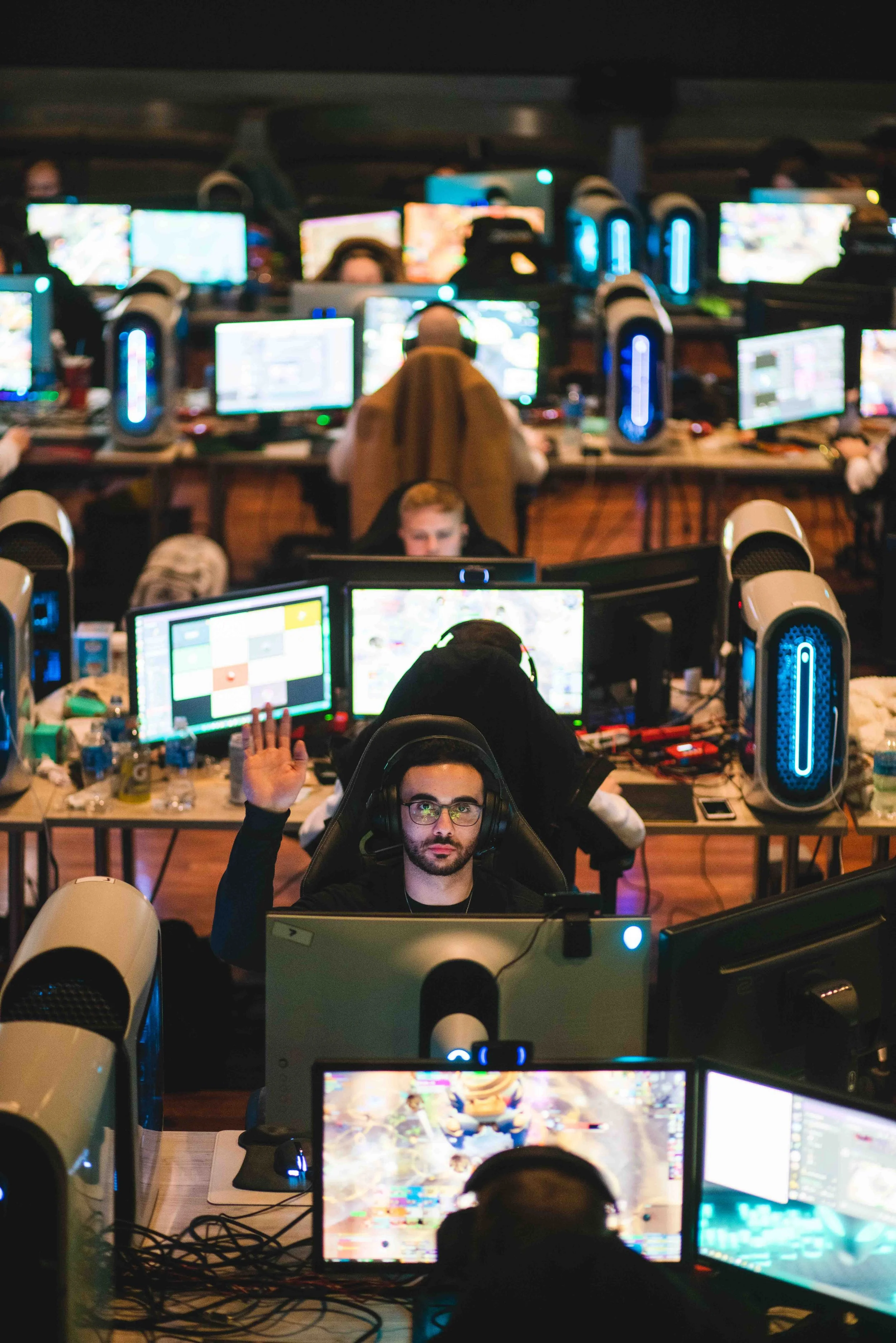 Game players in a large gaming tournament hall with multiple screens and gaming computers.